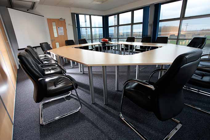 Empty modern meeting room with a U-shaped table, black leather chairs, and large windows showing an outdoor view