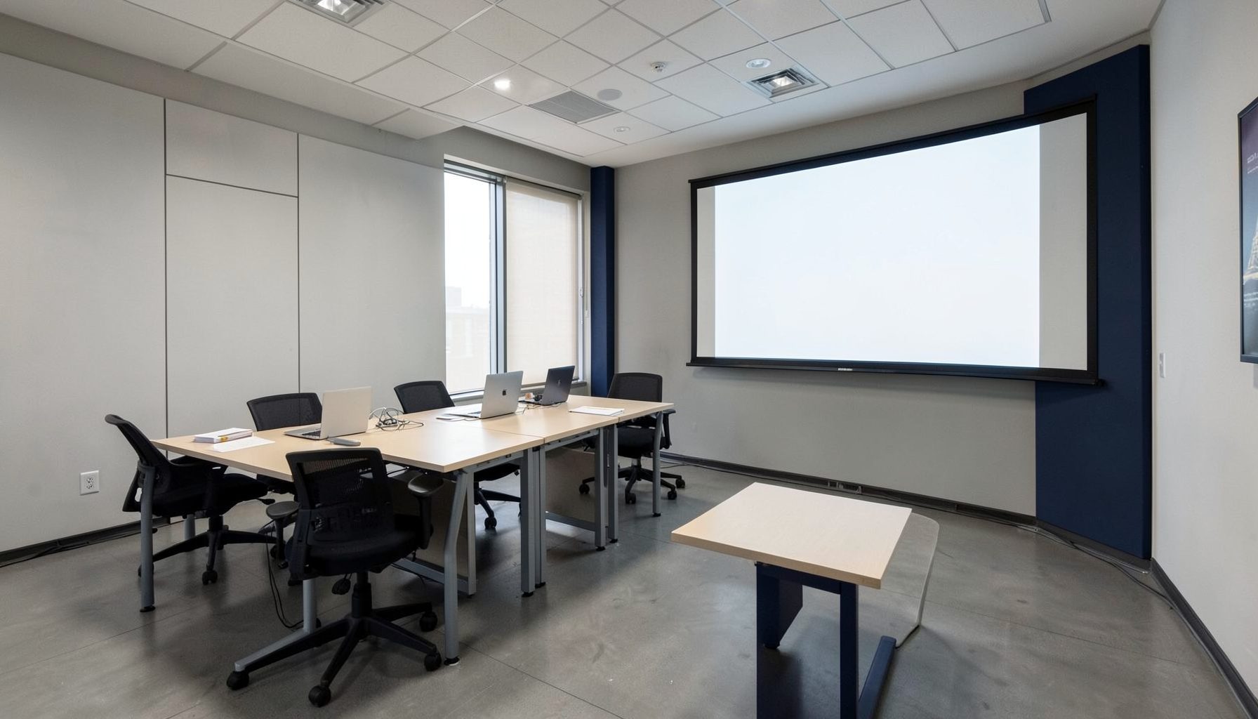 Empty conference room with a long table, office chairs, laptops, and a large blank projector screen